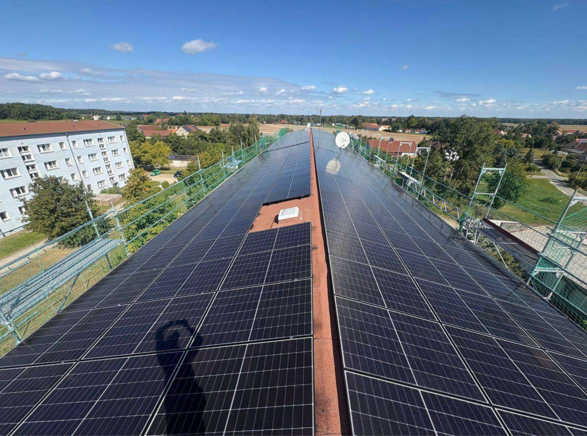 Originalfoto Lausitz K15: großflächige PV-Modulreihen in langer Dachperspektive, Wohngebäude links und blauer Himmel